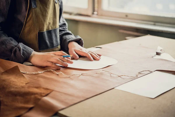 A young guy in a leather workshop transfers a pattern from paper to leather — Stock Photo, Image