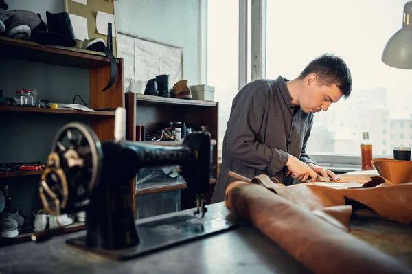 Un joven zapatero en su taller cose cuero en una máquina de coser, hace zapatos originales a pedido — Foto de Stock