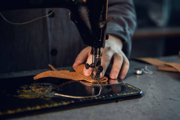 Close-up photo of a high-quality thread seam on a piece of brown genuine leather. Hands of a tailor and a sewing machine