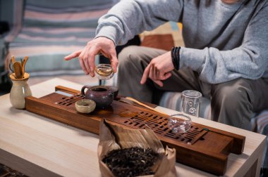 Çin çay içme geleneği yakın plan. Bir erkek eli, kilden yapılmış bir çaydanlığı tutar ve fincanlara lezzetli çay döker..