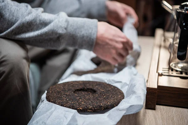 A chinese tea ceremony master holds a raw aged piece of tea cake in the interior of an oriental store.