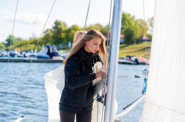 Güzel sarışın bayan sporcular yelkeni yatın direğine bağlamak için ipleri çekiyorlar.