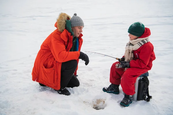 A young father teaches his son the basics of winter fishing on the ice of a lake in the village