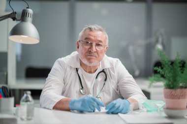 Kliniğin etkileyici baş doktoru ofisinde oturup kameraya poz veriyor.