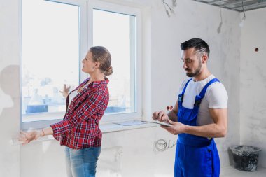 Müşteri tulumlu müteahhitle konuşur. Bir deftere yazıyor.