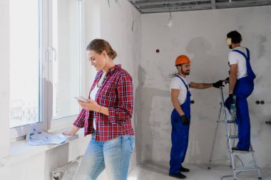 Bir müşteri pencerenin yanında durur ve belgeleri inceler, arka plandaki ustabaşı çalışır.