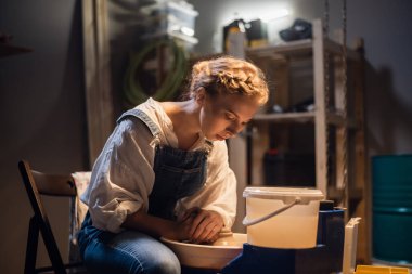 Genç sarışın çömlekçi kız atölyesinde çömlekçi çarkında vazo yapmaya başlıyor..