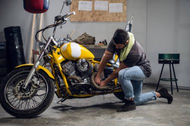 Tişört ve kot giyen modern genç bir adam tamirhanede ya da garajda bisiklet kontrolü yapıyor..