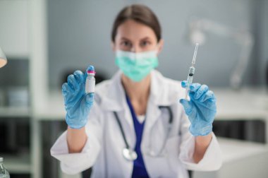 Tatlı kız terapist kameraya şişede yeni bir aşı gösteriyor. Klinikteki bir masada oturuyor.