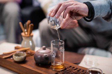 Geleneksel bir oryantal çay ayininin yakın çekimi. Bir adam mataradan tadım bardağına siyah olgun çay döküyor. Bulanık arkaplan.