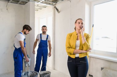 Müşteriler telefonla konuşuyor, inşaatçılar çimento yoğuruyor.