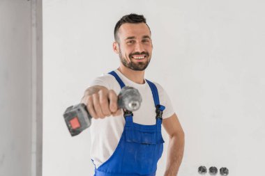 Neşeli işçi kameraya matkapla işaret ediyor.