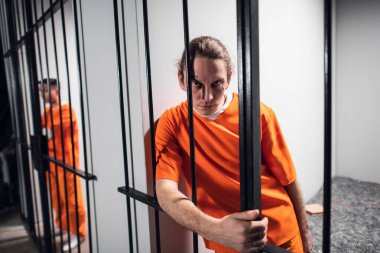 Dövmeli vahşi suçlu manyak demir parmaklıkları tutuyor. Bir hapishane hücresinde yakın plan bir portre..