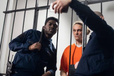 Maksimum güvenlikli bir hapishanede gardiyanlar hücrede oturan suratında dövmesi olan bir mahkumla selfie çekerler..