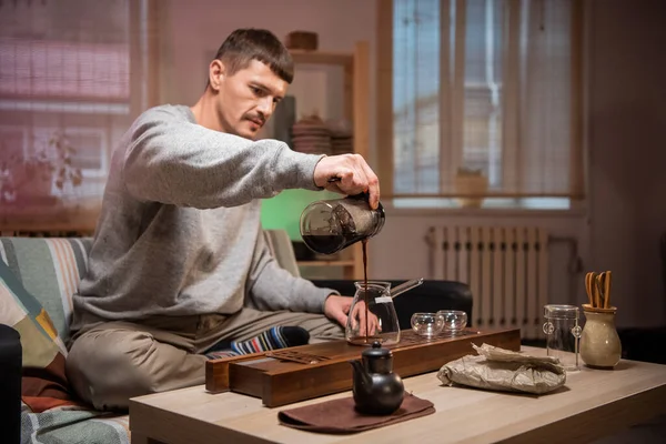 A man waits for guests and prepares authentic chinese tea using a tea ceremony kit. Brews ripe raw tea leaves in hot water according to instructions from the tea master.