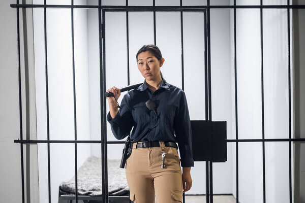 Asian guard in uniform In full armor with a baton and a pistol on the background of a prison cell