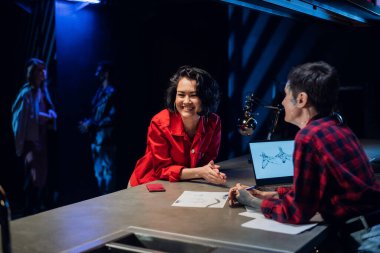 Bir kız genç bir dövme sanatçısıyla konuşur ve kağıda çizilen çizimlere dayanarak dövme seçer..