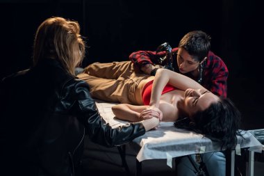 Genç ve güzel bir sanatçının dövmesi sırasında kız arkadaşı müşterilerin elini tutar.