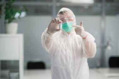 Koruyucu kıyafetli bir sıhhiye elinde bir şişe aşı tutuyor.