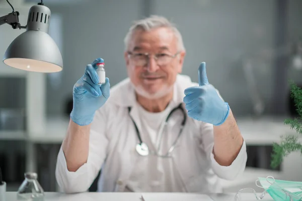 Yaşlı, deneyimli, güvenilir bir doktor kameraya koronavirüs aşısını gösteriyor. Nüfusun covid-19 'a karşı aşılanması kavramı