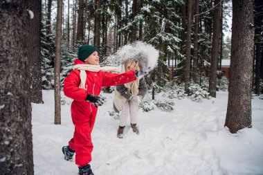 Kış tulumlu oğlum ve kürklü annem kışın ormana kar atıyor.
