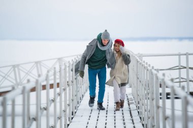 Genç bir adam ve kadın kış tatilinde birlikte vakit geçiriyorlar, nehirde karla kaplı bir iskelede yürüyorlar.