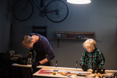 Genç bir baba ve küçük oğlu marangozların atölyesinde ağaçtan oyuncak yapıyorlar..