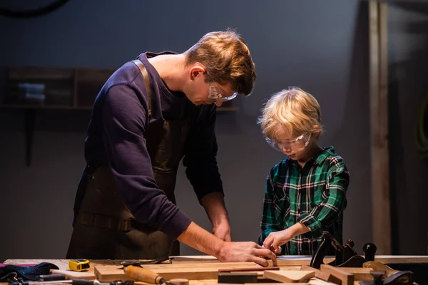 Genç bir baba ve küçük oğlu marangozların atölyesinde ağaçtan oyuncak yapıyorlar..