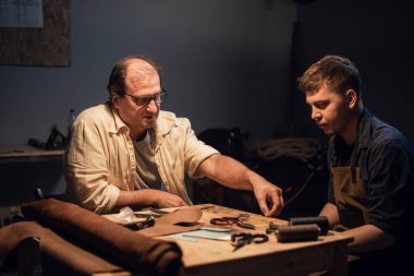 Yaşlı bir kunduracı ve çırağı atölyelerinde çeşitli aletlerle el yapımı ayakkabılar yapıyorlar..