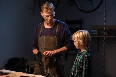 Deneyimli bir marangoz atölyede oğluna çeşitli aletlerin çalışmalarını gösterir..