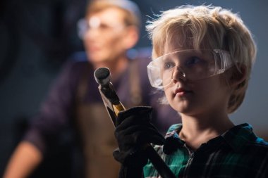 Marangoz dükkanındaki sevimli sarışın çocuk koruyucu gözlüklü ve kulaklıklı çekiçli, portresi olan..