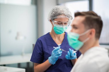 Hastanedeki laboratuvarda, bir hemşire erkek bir hastanın koluna iğne yapar.