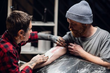 Dövme sanatçısı dövmeyi yaptıktan sonra genç adamın elini ince bir katman petrol jeliyle bandajlıyor..