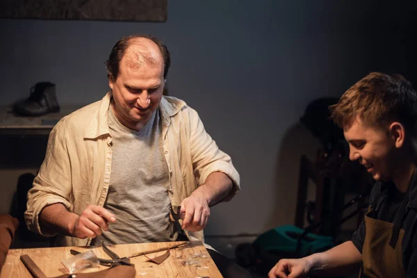 Een leuke jonge kerel wil een cadeau te maken met zijn eigen handen, een ervaren schoenmaker helpt hem schoenen van leer. — Stockfoto