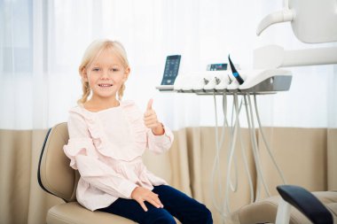 Diş hekiminde küçük güzel bir bayan çocuk kameraya bakıyor ve gülümsüyor.