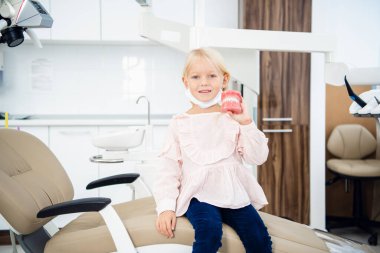 Ellerinde yapay bir çeneyle oturmuş, dişlerinin arasında gülümseyen bir bebek.