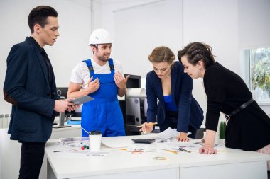 Ofiste bir planı tartışan çok ırklı inşaatçılar, inşaatçılar, girişimciler ve mimarlardan oluşan bir grup.