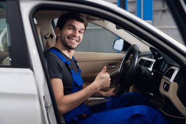 Tamirci arabada oturuyor ve parmağını gösteriyor.