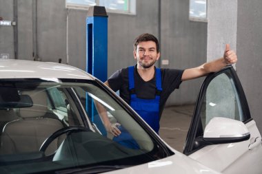 Yakışıklı bir tamirci arabanın yanında duruyor.