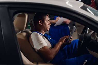 Bir tamirci ve iş arkadaşı bir arabayı inceliyor.