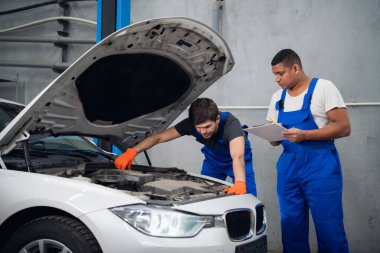 Tamirciler bir arabanın motorunu tamir eder ve rapor yazar.