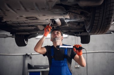 Makinist arabanın altını kontrol eder ve bir el feneri tutar.