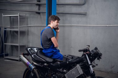 Bir tamirci bisiklette oturmuş müşteriye sesleniyor.