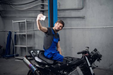 Bir tamirci motosikletle fotoğraf çeker.