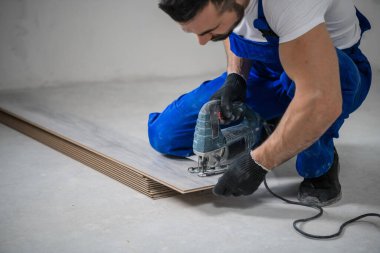 Mavi üniformalı tamirci yapbozla kaplama kesiyor.