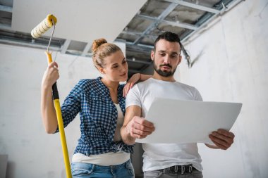 Evli bir çift daire planını ellerinde tutuyor ve gülümsüyor.