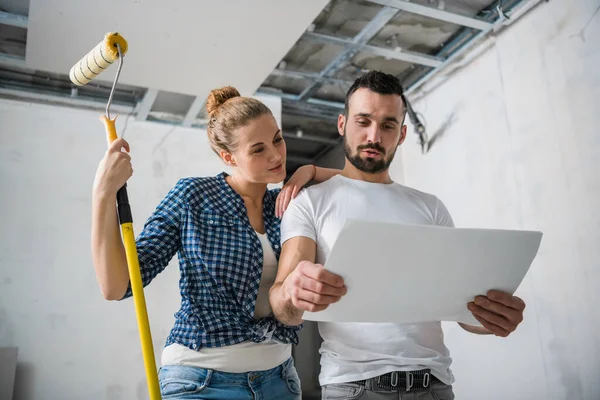 Evli bir çift daire planını ellerinde tutuyor ve gülümsüyor.