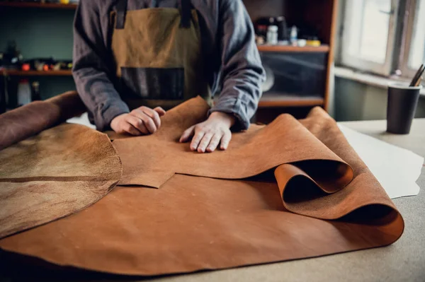 Before making shoes out of leather, a young guy lays them out on the table in the workshop