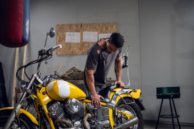 Tişört ve kot giyen modern genç bir adam tamirhanede ya da garajda bisiklet kontrolü yapıyor..