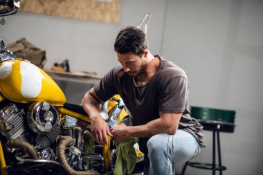 Tişört ve kot giyen modern genç bir adam tamirhanede ya da garajda bisiklet kontrolü yapıyor..